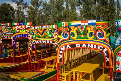 Trajineras decoradas con flores y colores vibrantes, navegando por los canales de Xochimilco en la CDMX.