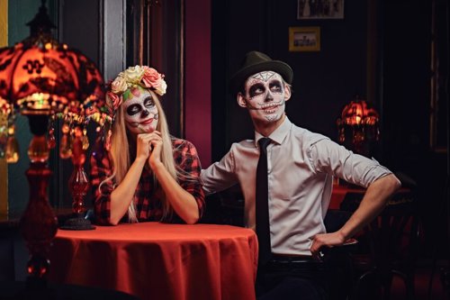 Pareja disfrazada de catrinas para el Día de Muertos: ella con corona de flores y camisa a cuadros, él con camisa blanca y sombrero